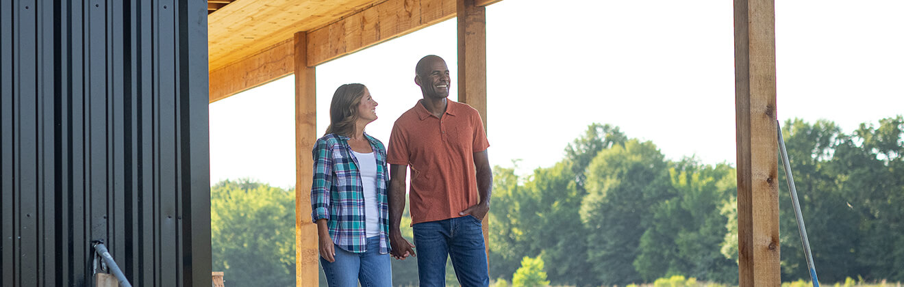 A couple standing on the porch of their under-construction rural home.